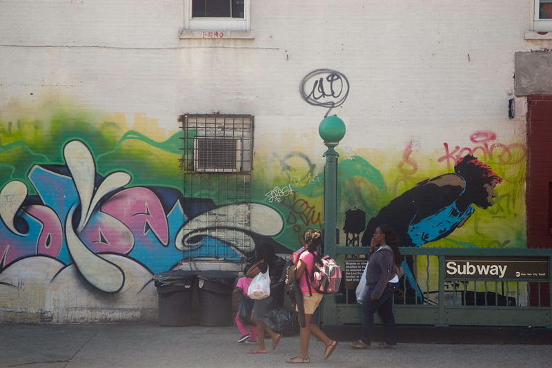 People walk past two murals in very different styles.