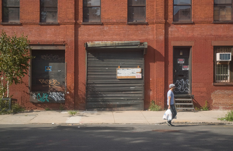 A man carrying groceries past an old brick building.