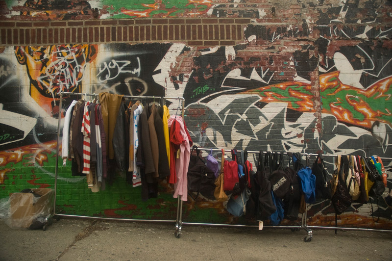 Sale racks, outside against a wall with graffiti