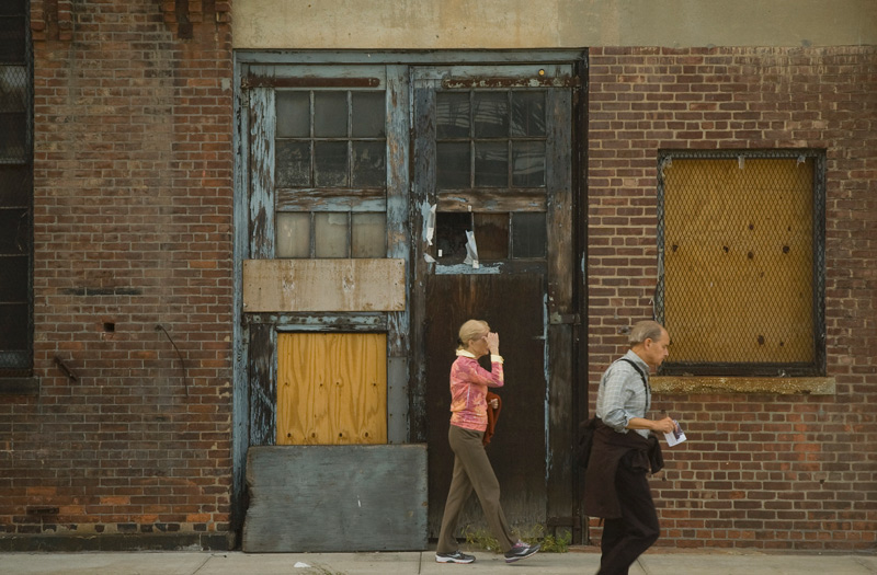 Two people walking past an old brick building.