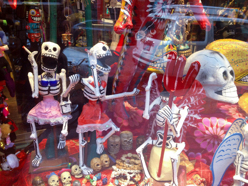 A colorful store window with Day of the Dead figures.