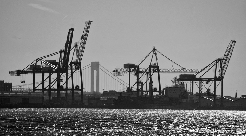 A river, loading cranes, and the Verrazano Narrows Bridge.