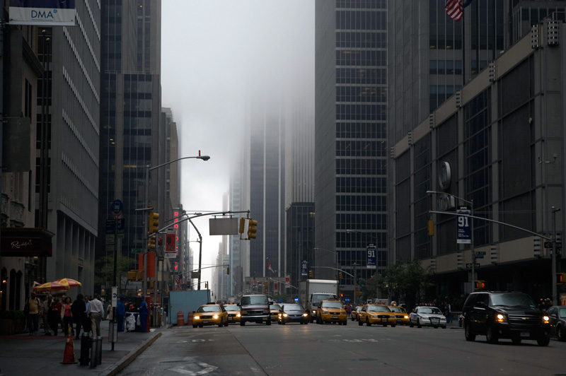 Mist and fog cover skyscrapers and darken a street.