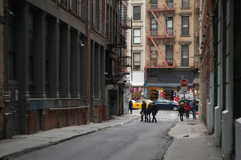 People crossing the intersection of a street and alley.