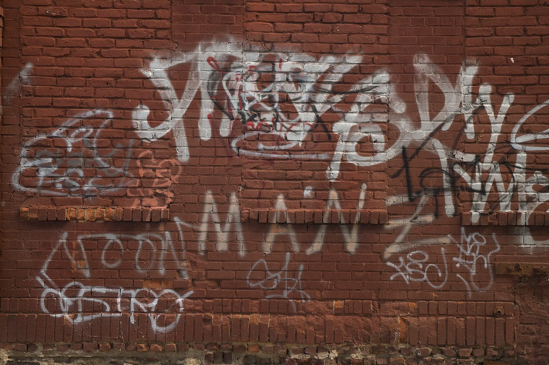 Brick wall with graffiti tags, 'MANZ' among them.