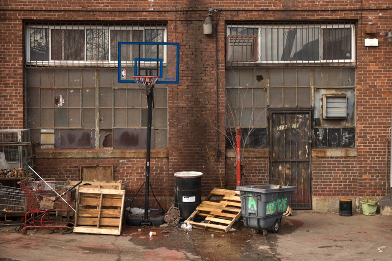 Backside of a building, with a basketball hoop and debris.