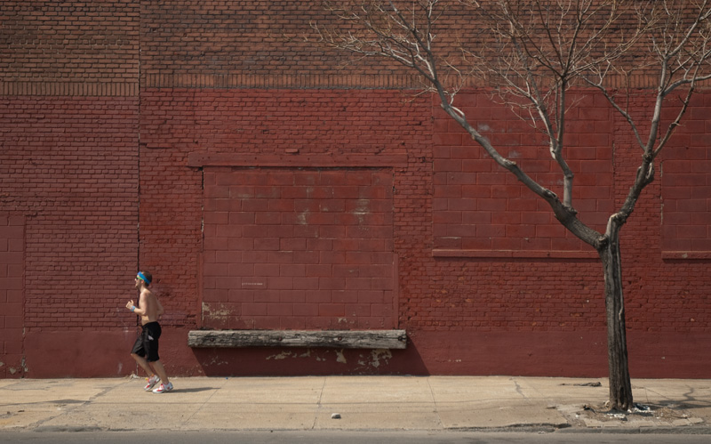 A runner passing a brick wall and a barren tree.