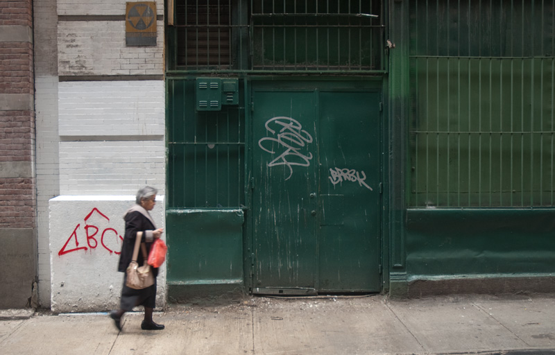 An older woman walking on an alley sidewalk.