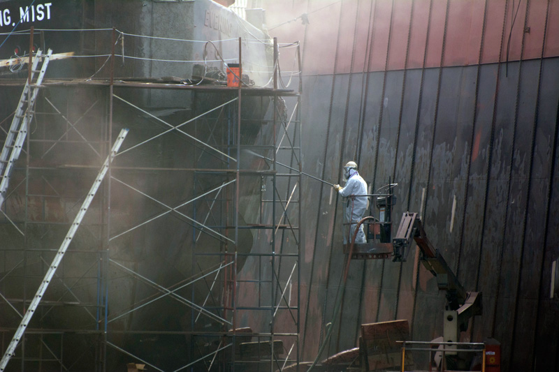 A worker powerhosing a tugboat.