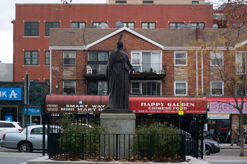 A statue of Athena, facing apartments and storefronts.