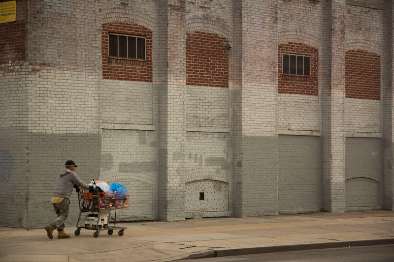 A man pushing a shopping cart of empty bottles.