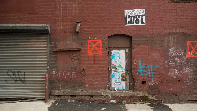 An old brick building, with graffiti tags and street art posters.
