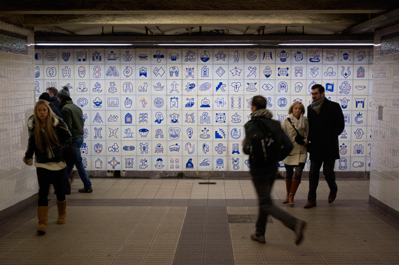 People in a subway station hall decorated with tiles.