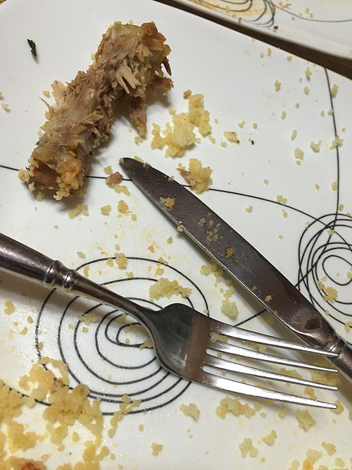 The bone of a chicken thigh and some couscous are left from a meal.
