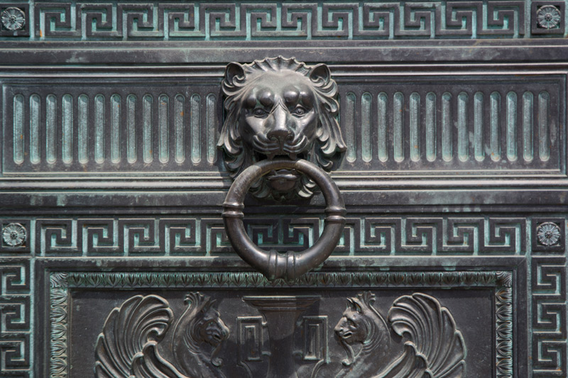 A lion head and door pull on an ornate bronze door