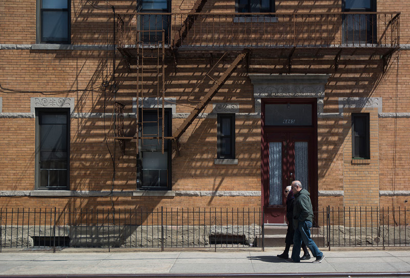 A couple pass an apartment building cast in fire escape shadows