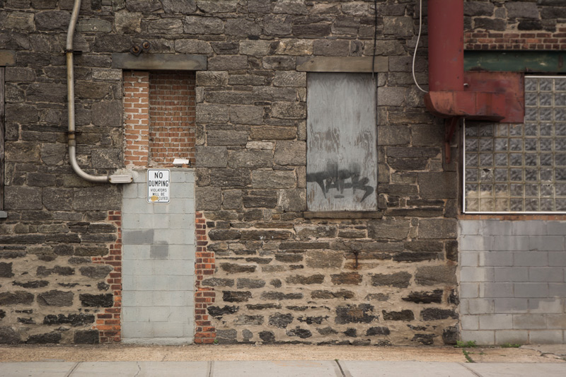 A building wall, made of stone, with ducts and doors.