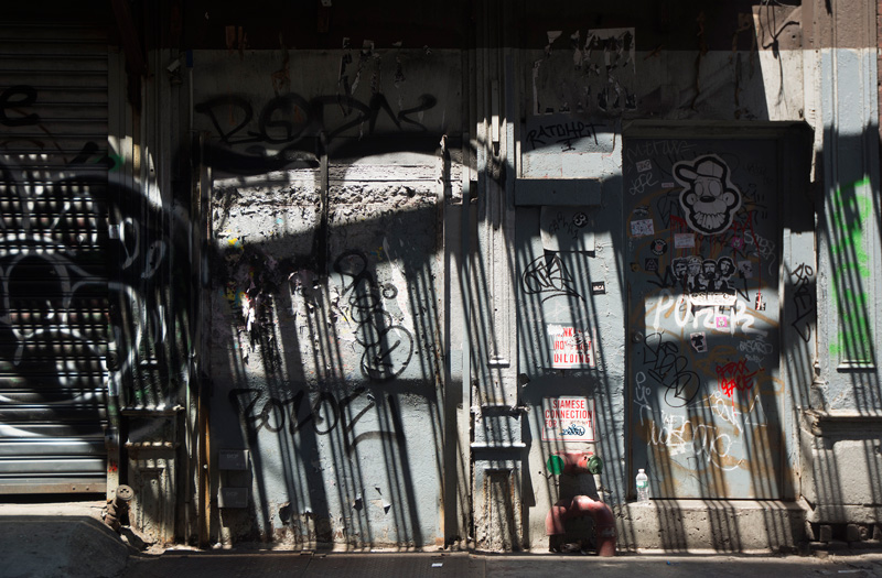 An alley wall, striped with shadows from a fire escape.