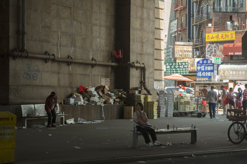 A woman sits on a bench under the Manhattan Bridge.