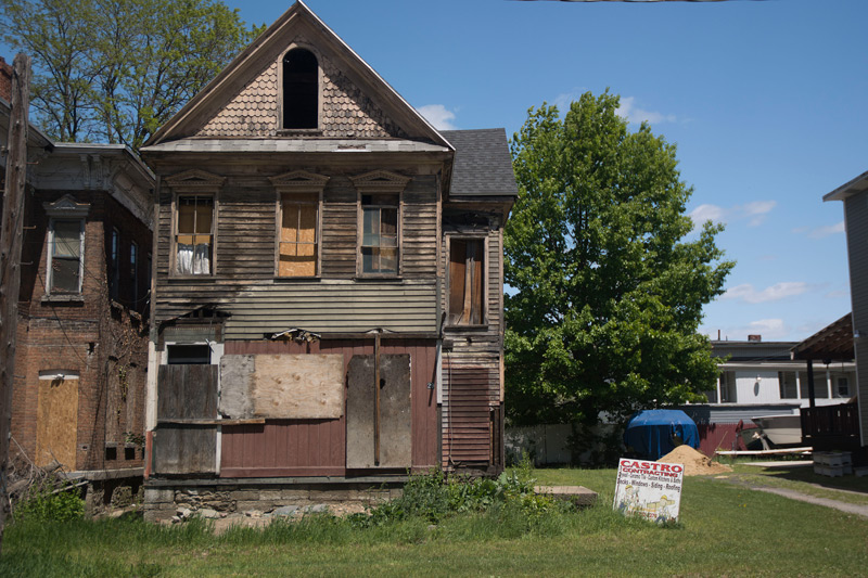 A wood house in really poor shape, with a sign indicating improvements.