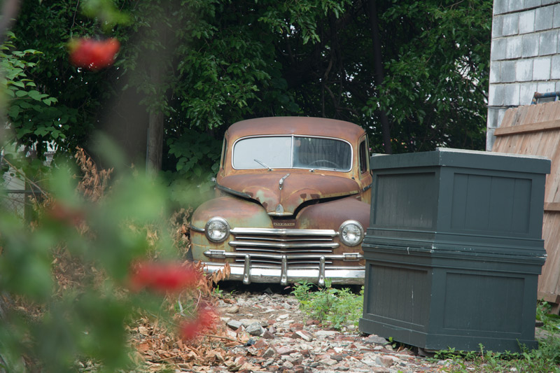 A classic car, rusting in a back yard.