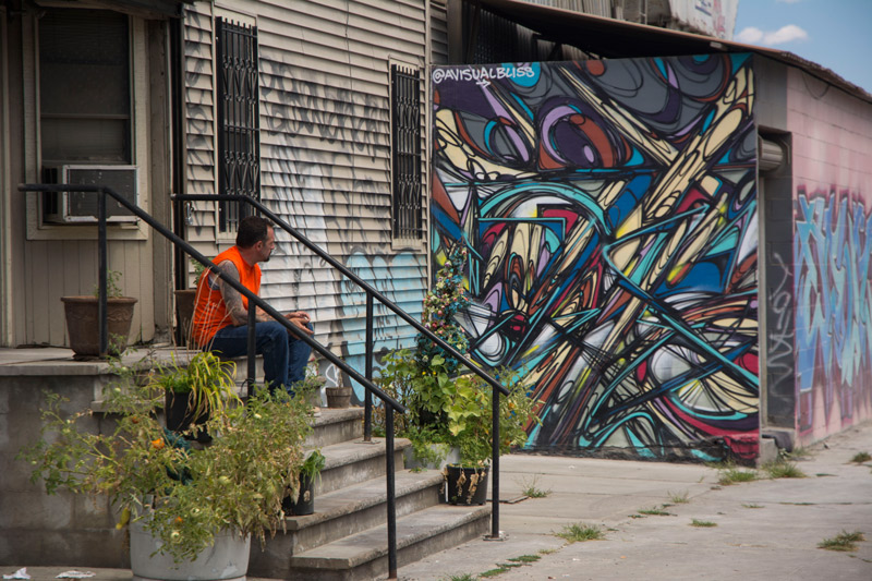 A man sitting on a stoop next to psychedelic street art.