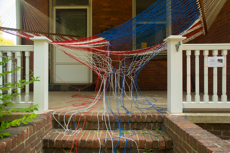A flag-like sculpture of red, white, and blue threading, as a loose hammock.