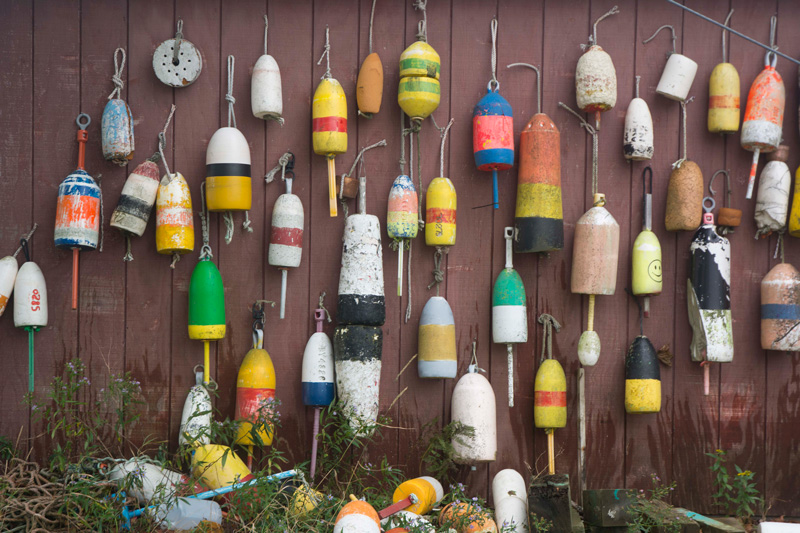 Dozens of colorful lobster trap buoys hanging on a wall.