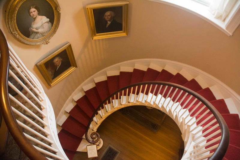 A curved staircase, with portraits on the wall.