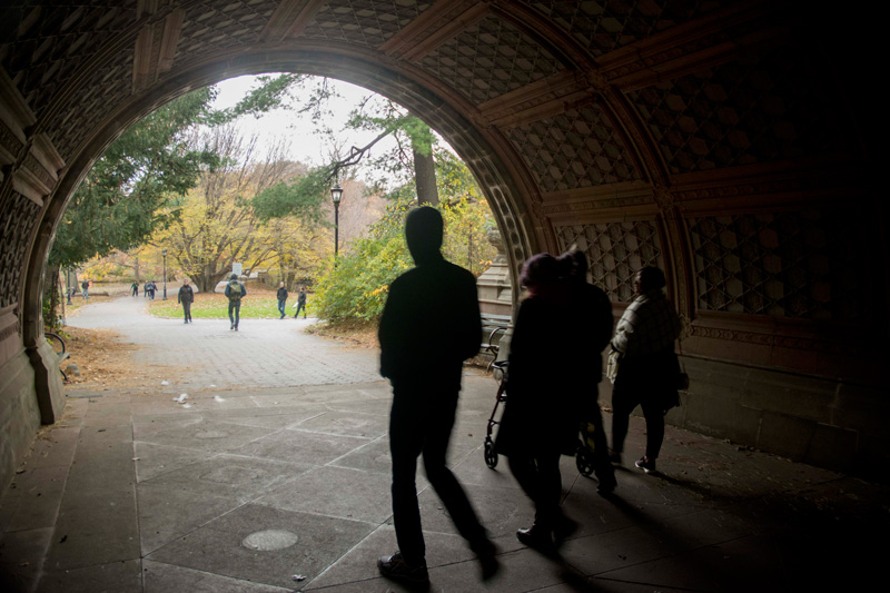 A small group of people walking into sunlight from under an arch..