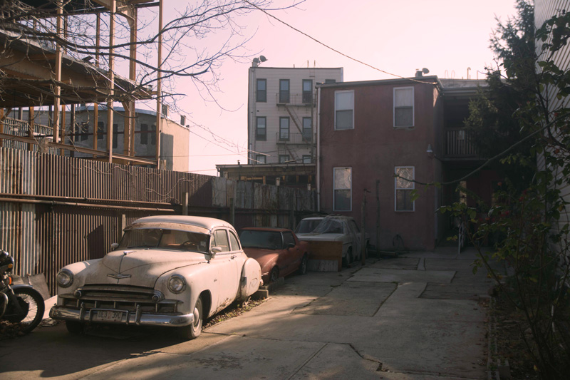 Junk classic cars in a lot behind a building.