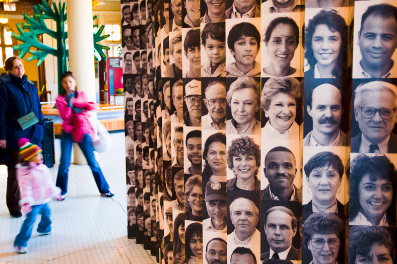 A wall of photos of Americans of diverse background, at Ellis Island.