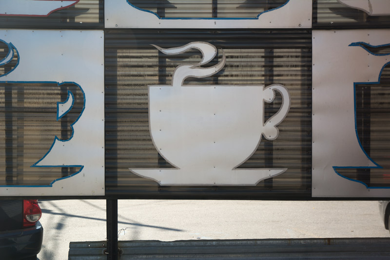 A metal diner sign with a silhouette of a steaming coffee cup.
