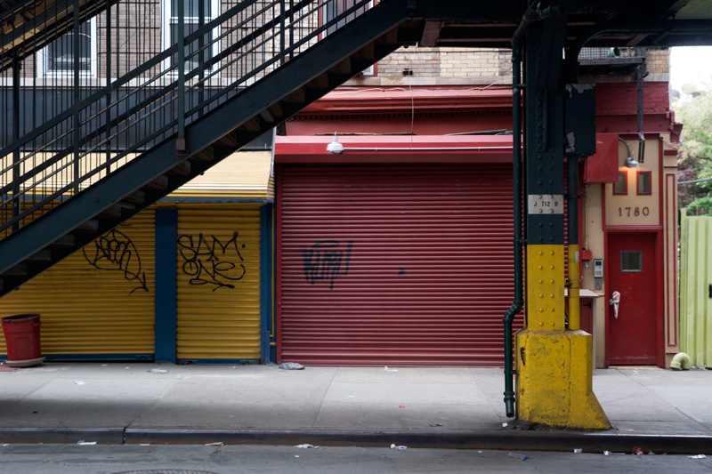 Shuttered storefronts beyond the stairs to an elevated subway station.