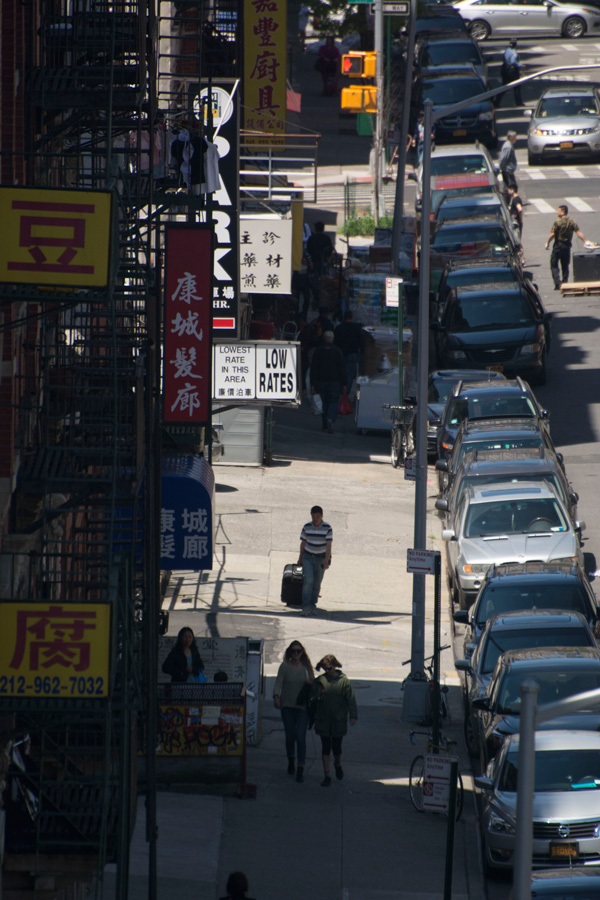 A pedestrian rolling a suitcase past a parking lot advertising low rates.