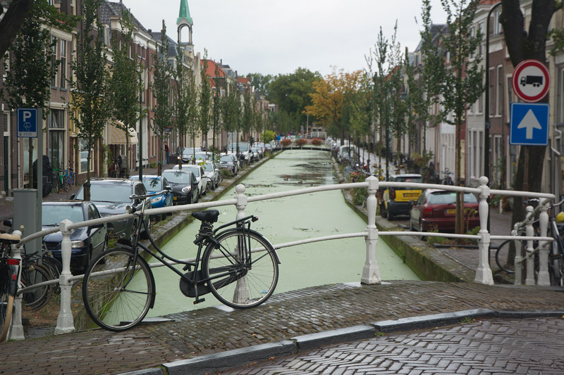 A bike locked to the railing of a bridge over a small canal.