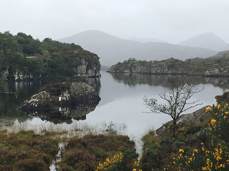 A lake, with cliffs and their reflections, as well as mountains in the background.