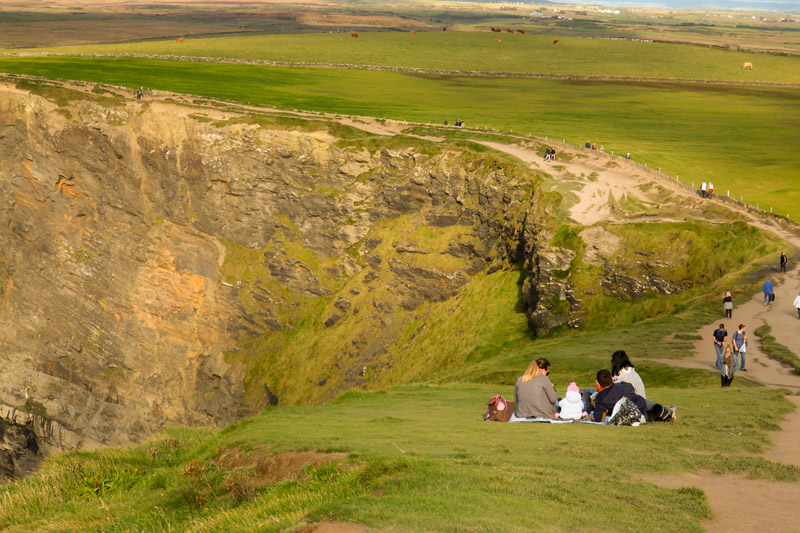 A couple and their young child enjoy the scenery of the Cliffs of Moher, sitting on a blanket.