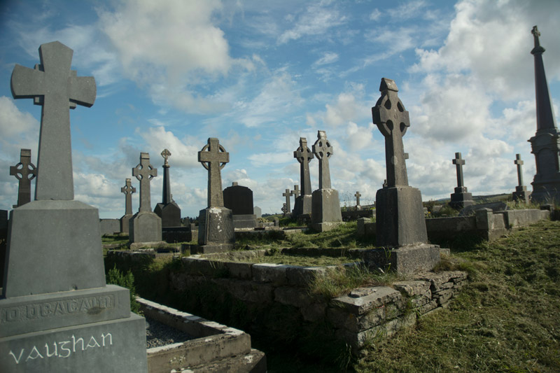 Twenty or more tombstones in a cemetery, each with a cross. The sky is blue.