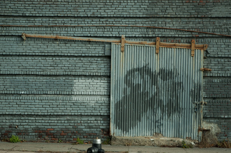 A brick wall, and its closed metal entrance, are all painted green.