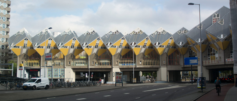 A row of apartments, set as downward tilting cubes, suspended over a roadway.