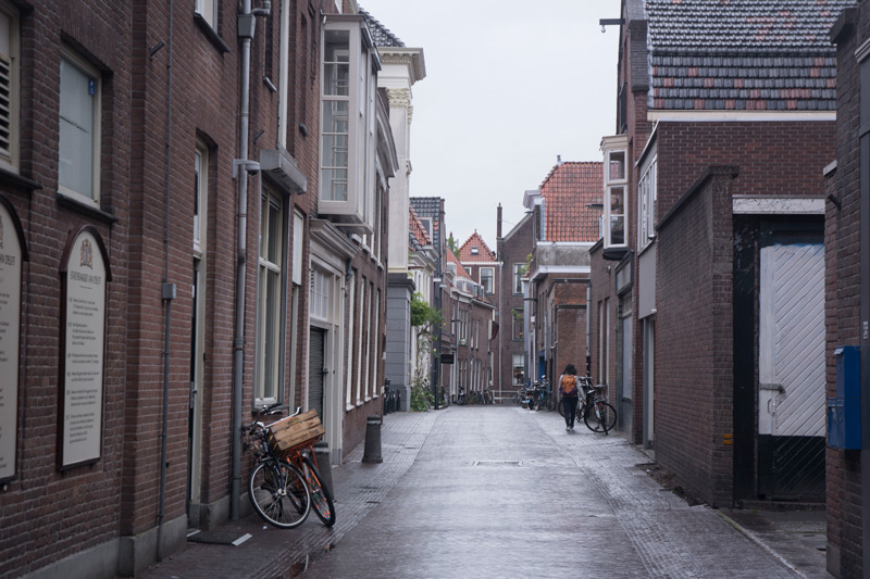 A small street, with old biuildings and locked bicycles, and a lone pedestrian.