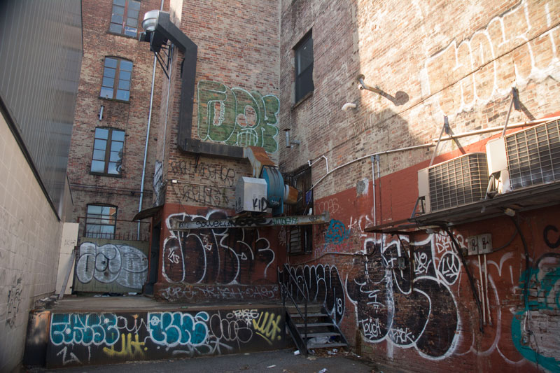 Graffiti tags cover the walls of an alley.