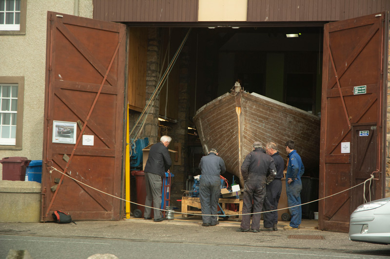 Men huddle around a boat being refurbished.