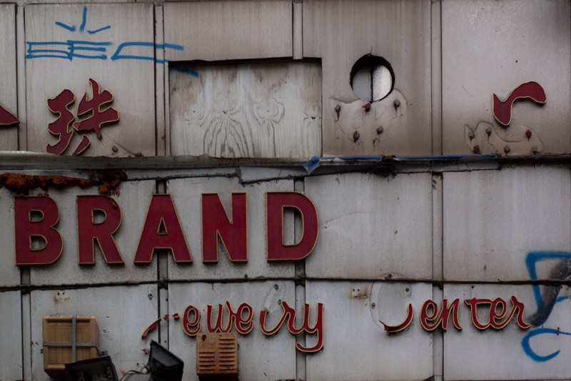 The photo shows a store sign with letter missing and plywood patches.