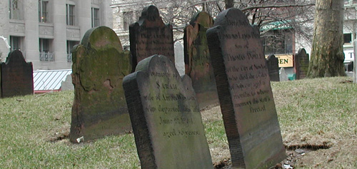 Old tombstones
in a grave yard surrounded by modern buildings.