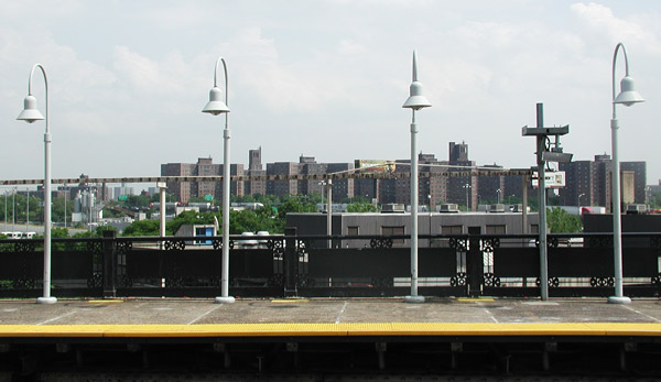 Four white lampposts on a concrete subway
platform; apartment complexes are visible in the
distance.