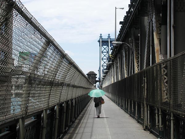 A solitary person with a parasol walks on
the pedestrian walkway, surrounded by fencing.