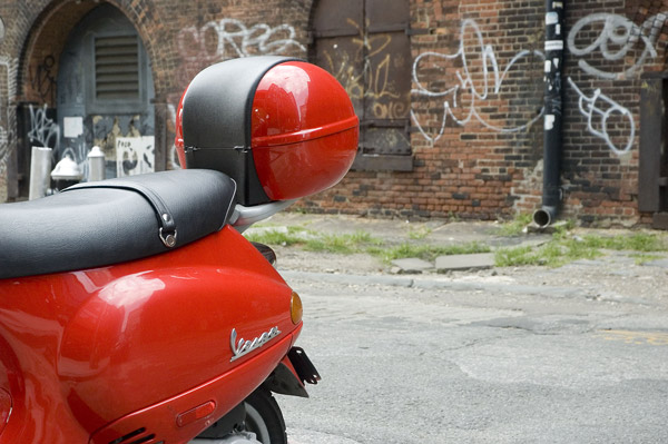 A red Vespa motorcycle on a street with brick walls and
graffiti