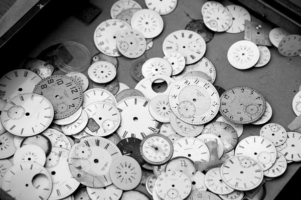 Scores of varied watch dials are laying in a box.